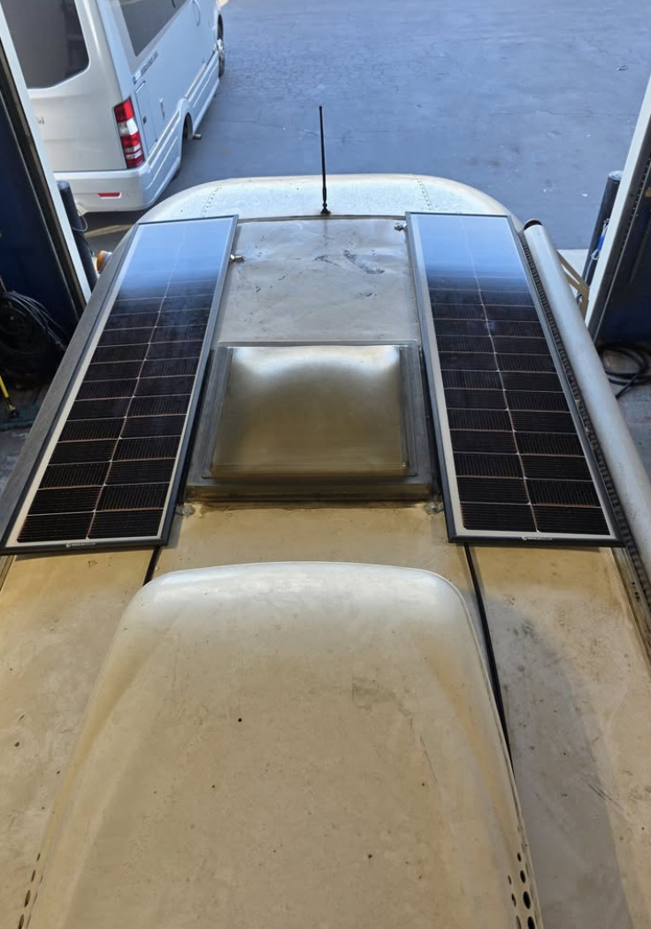 Two solar panels installed on an RV roof beside the vent